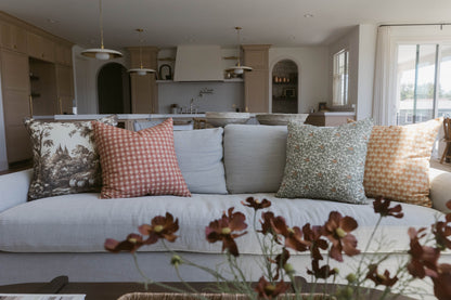 Four decorative pillows in varying patterns displayed on a light gray sofa in a kitchen-living space.