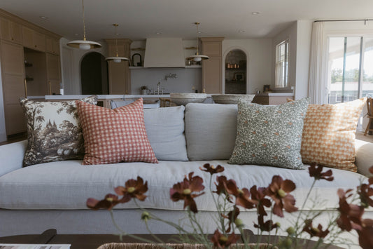 Four decorative pillows in varying patterns displayed on a light gray sofa in a kitchen-living space.
