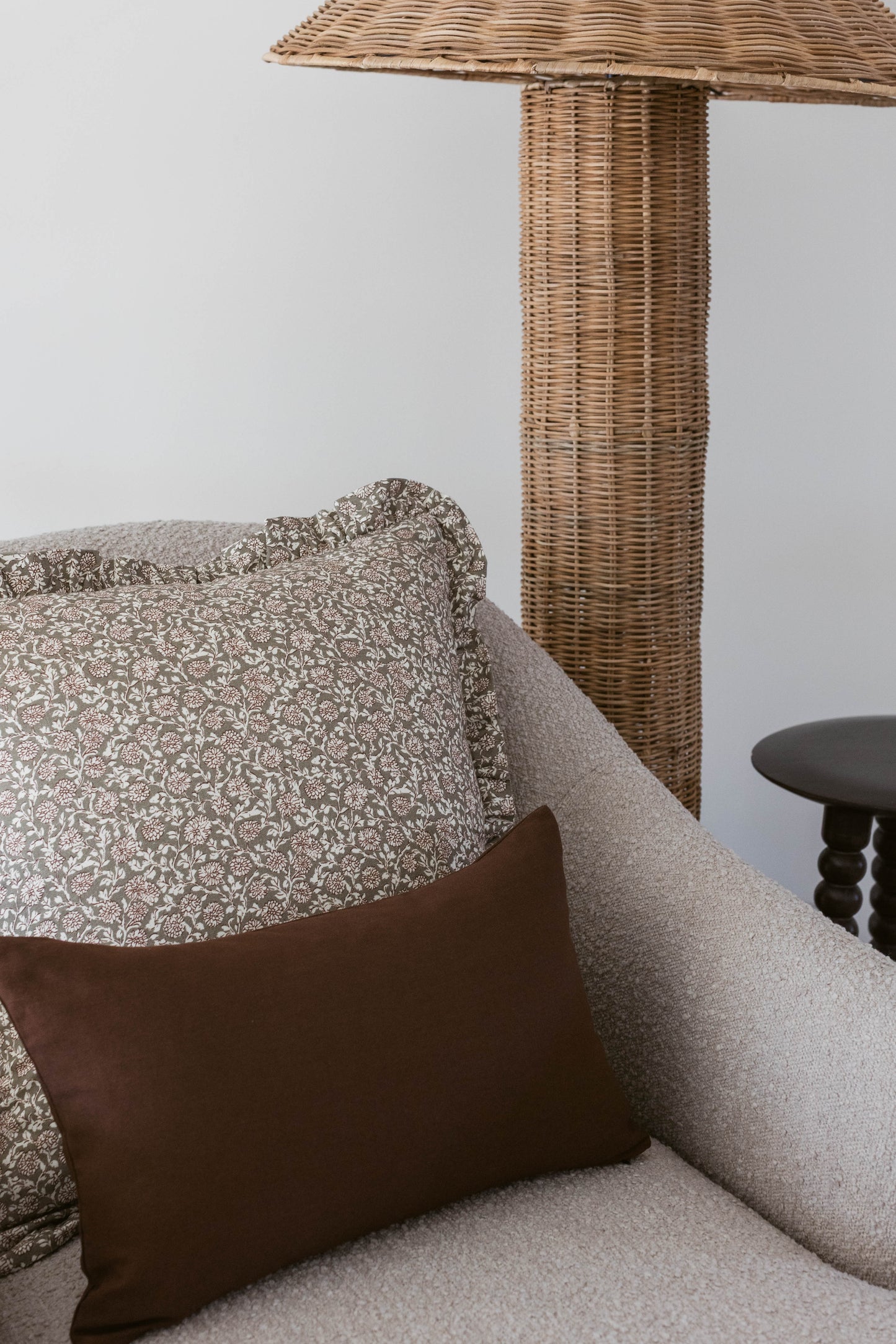 Brown and cream patterned pillow on gray upholstered chair with woven umbrella and dark side table.