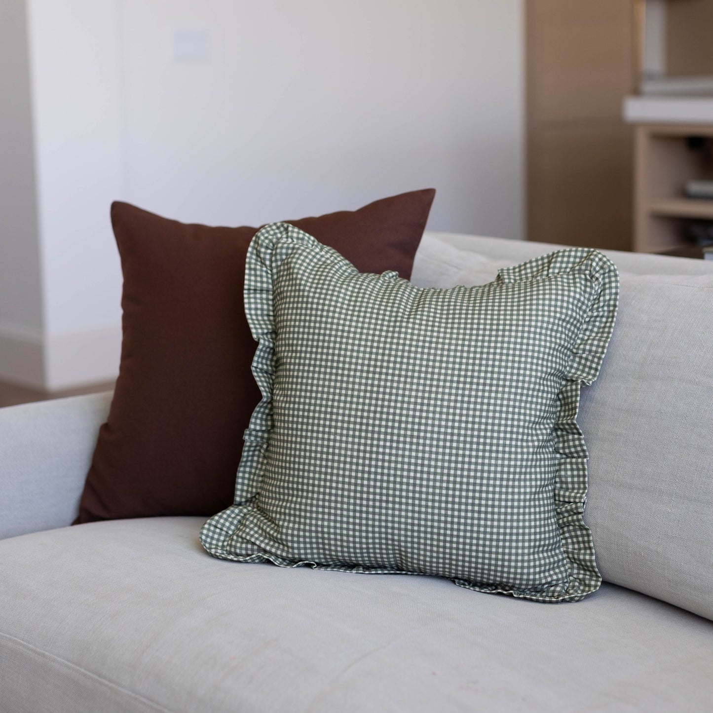 Green and white mini gingham pillow cover with ruffled edges displayed on a beige sofa.