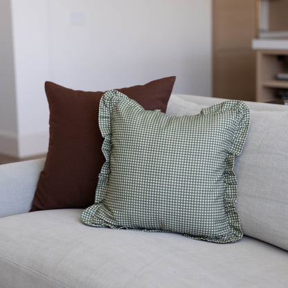 Green and white mini gingham pillow cover with ruffled edges displayed on a beige sofa.