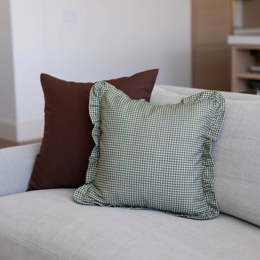 Green and white mini gingham pillow cover with ruffled edges displayed on a beige sofa.