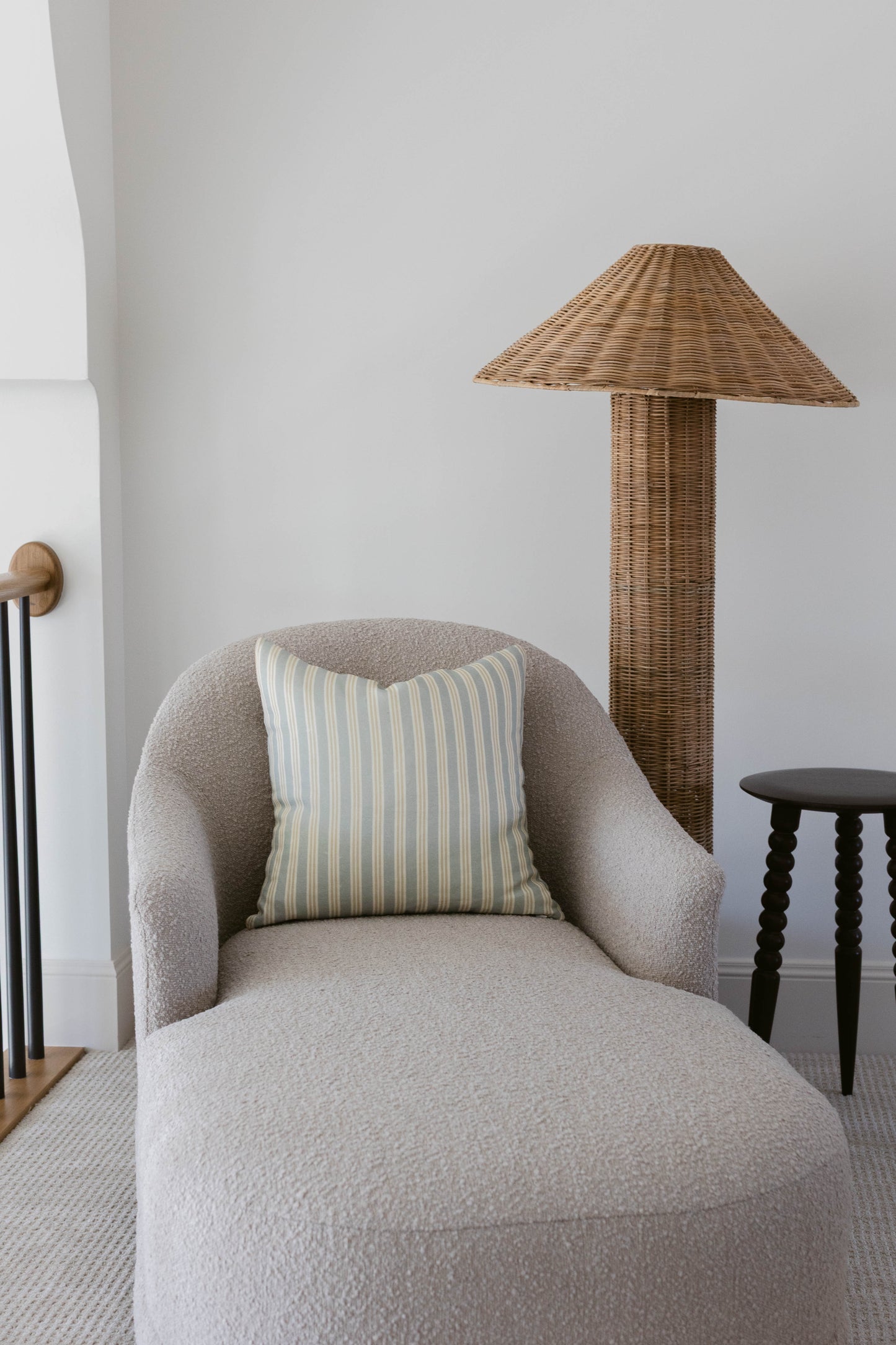 Striped cream and gray pillow on gray upholstered chair with curved arms in minimalist interior.