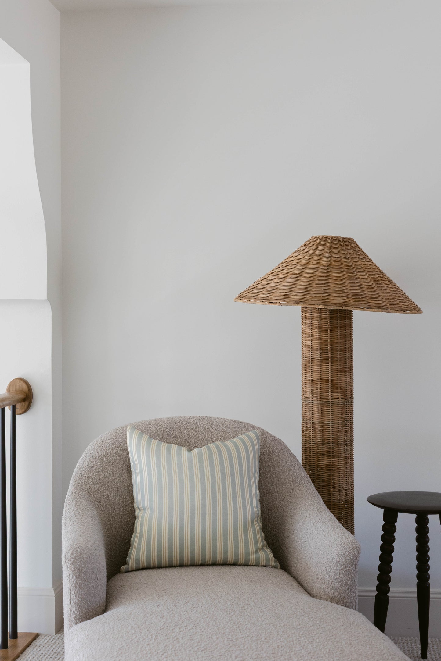 Woven rattan floor lamp with conical shade and cylindrical base next to gray upholstered armchair.
