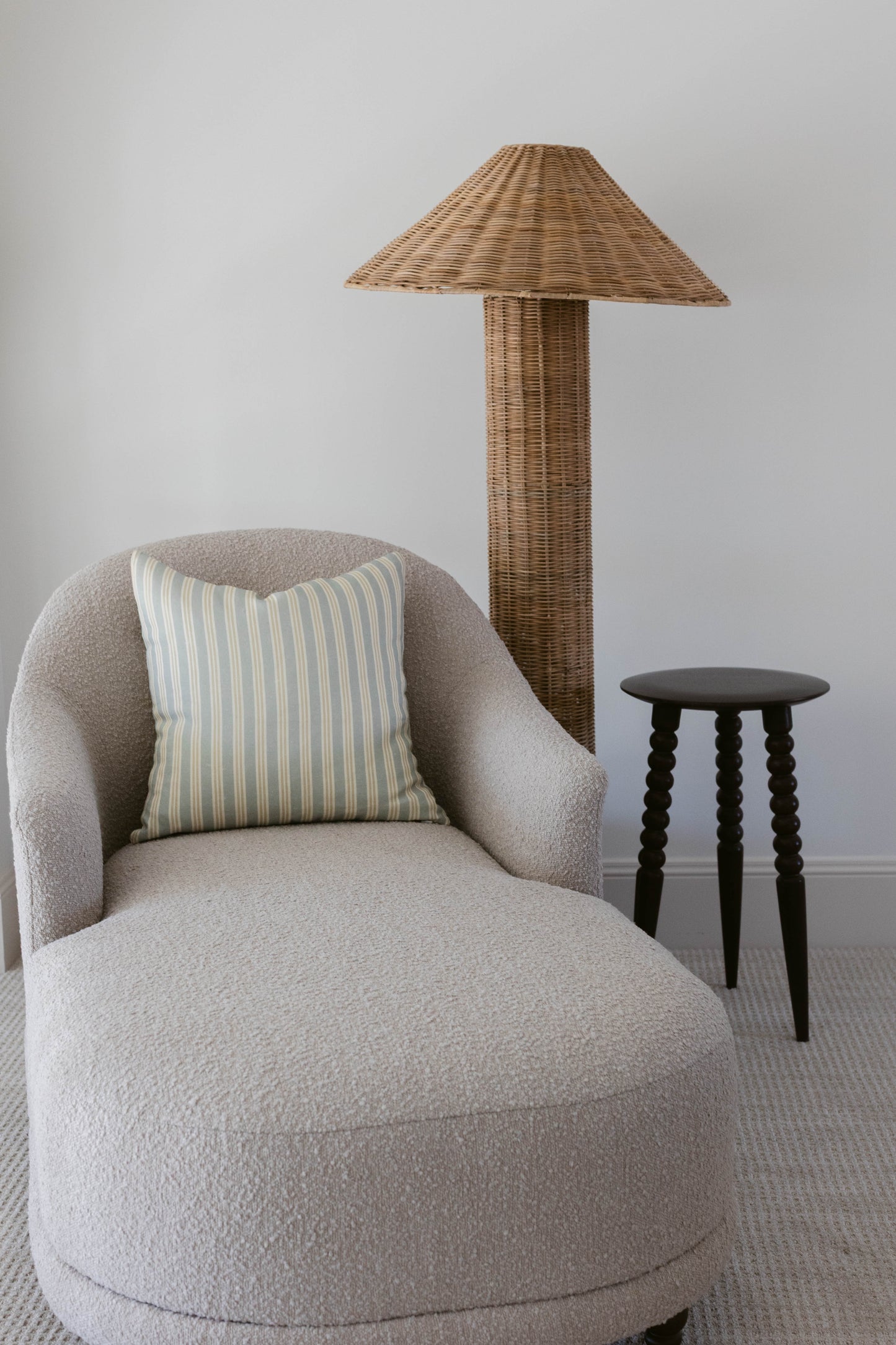 Beige curved armchair with striped pillow, woven rattan floor lamp, and black side table.