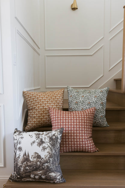 Red and white gingham pillow displayed on wooden stairs with coordinating patterned pillows.