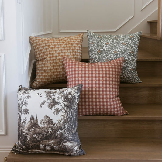 Orange and white plaid pillow with coordinating patterned pillows displayed on wooden stairs.