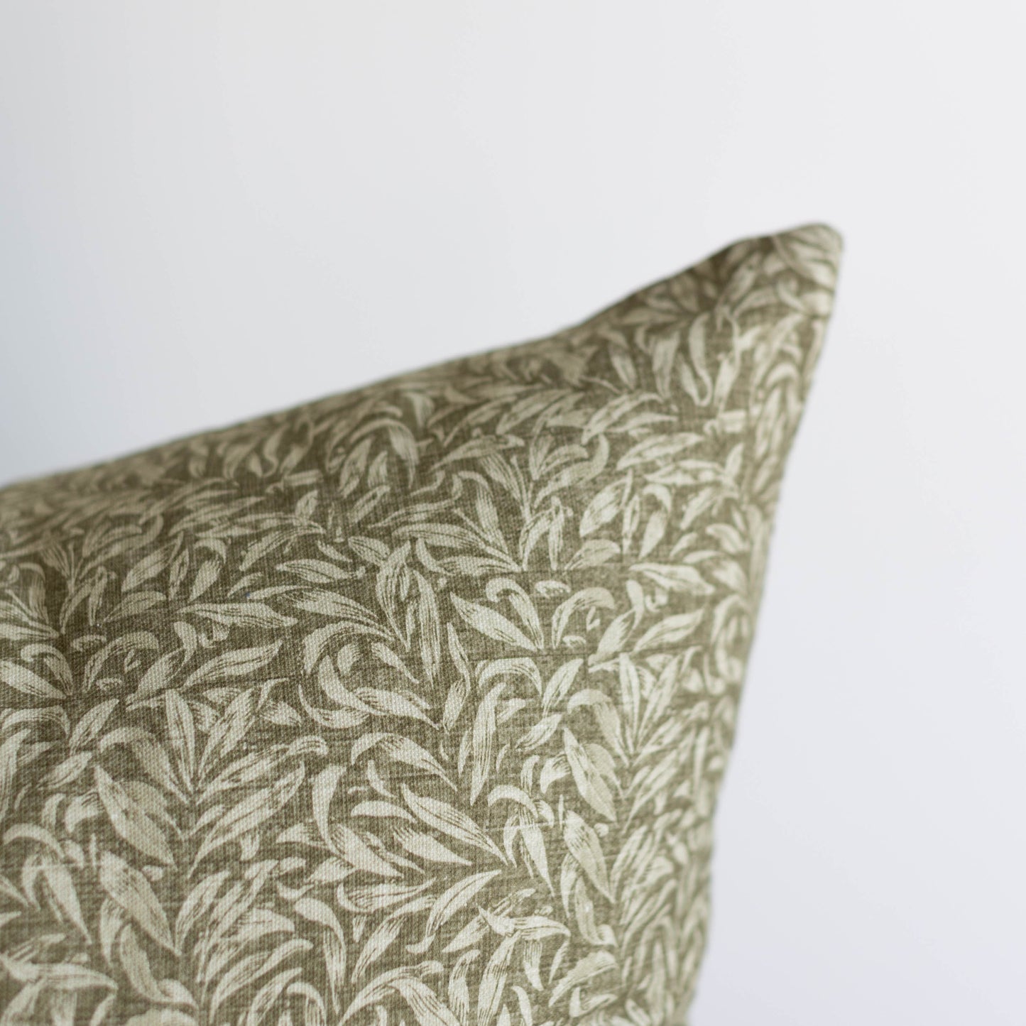 Green and cream leaf-patterned pillow with textured fabric, corner detail visible.