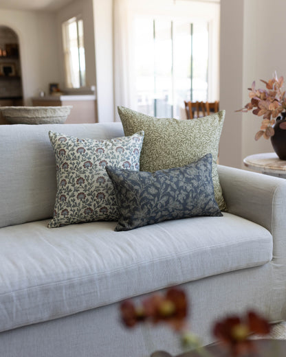 Three decorative pillows with multicolor leaf patterns in cream, green, and navy displayed on a light gray sofa.