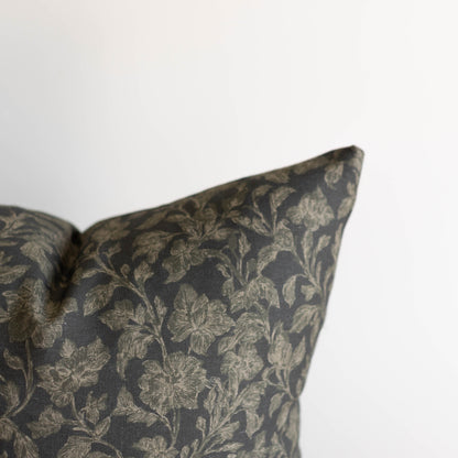 Charcoal pillow with cream botanical leaf pattern, corner detail visible against white background.