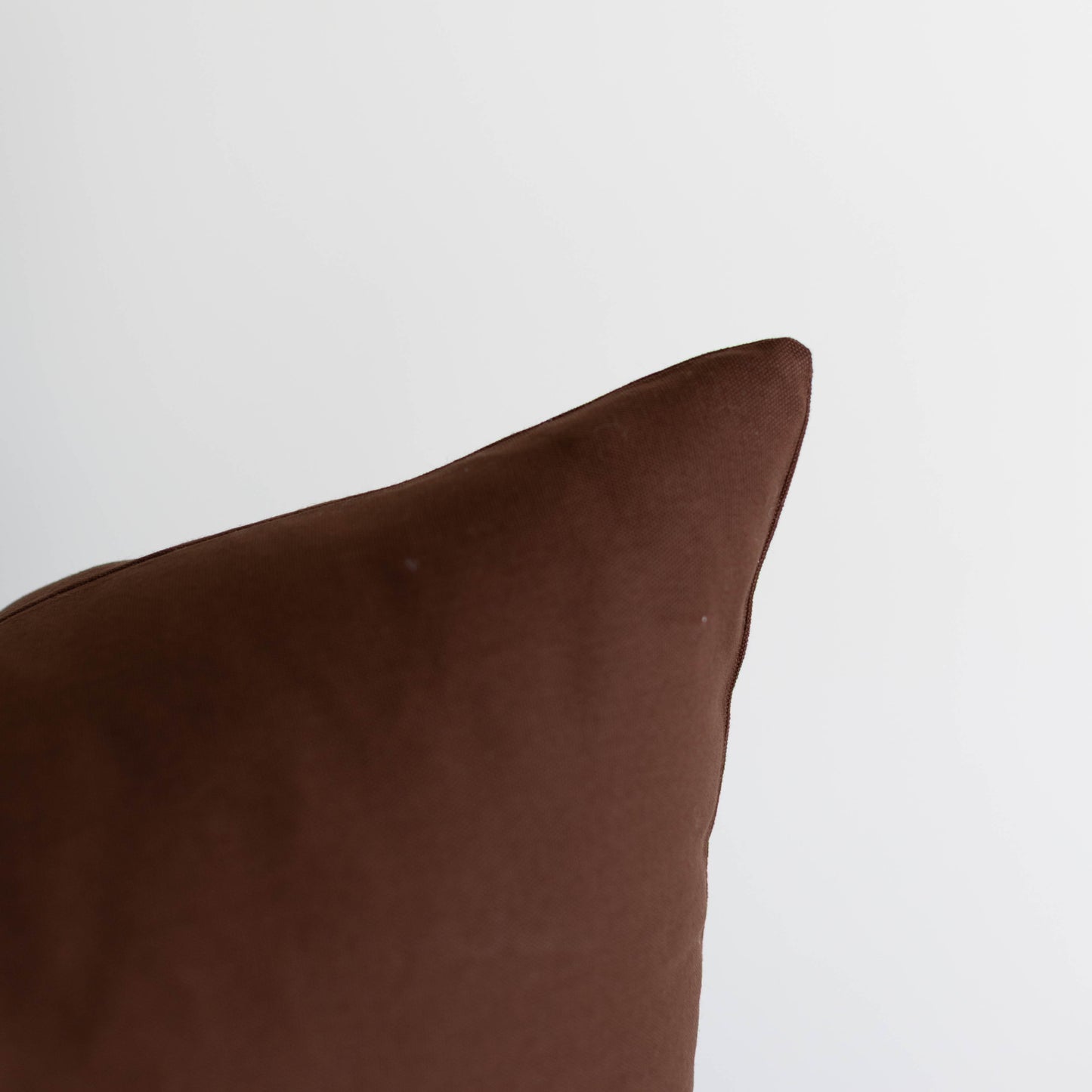 Dark brown rectangular pillow with a soft texture and curved corner detail against a light gray background.