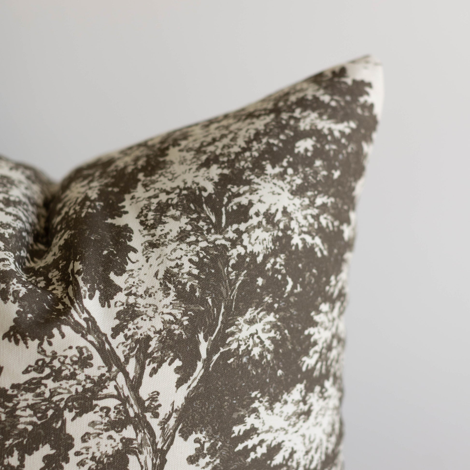 Charcoal and cream decorative pillow with tree silhouette pattern and textured weave fabric.
