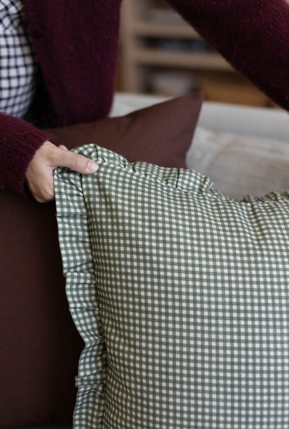 Green and white gingham cloth with ruffled edge held in hand.