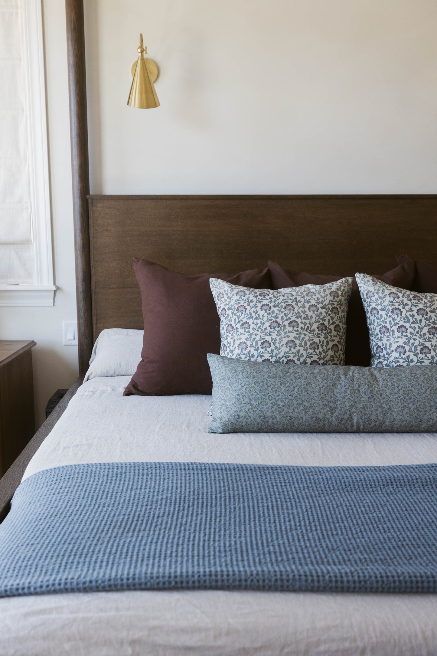 Brass cone pendant light hanging above a bed with blue patterned pillows and blanket.