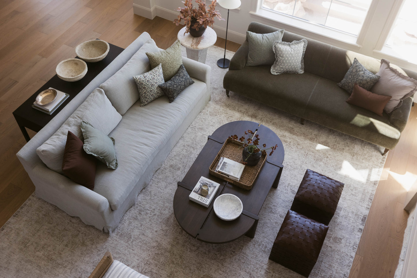 Overhead view of living room with light gray sofa, dark brown sofa, oval coffee table, and decorative pillows on neutral area