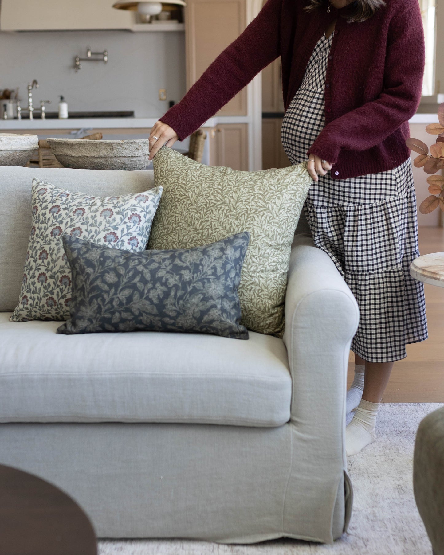 Three patterned throw pillows in green, blue, and neutral tones arranged on a cream-colored sofa.