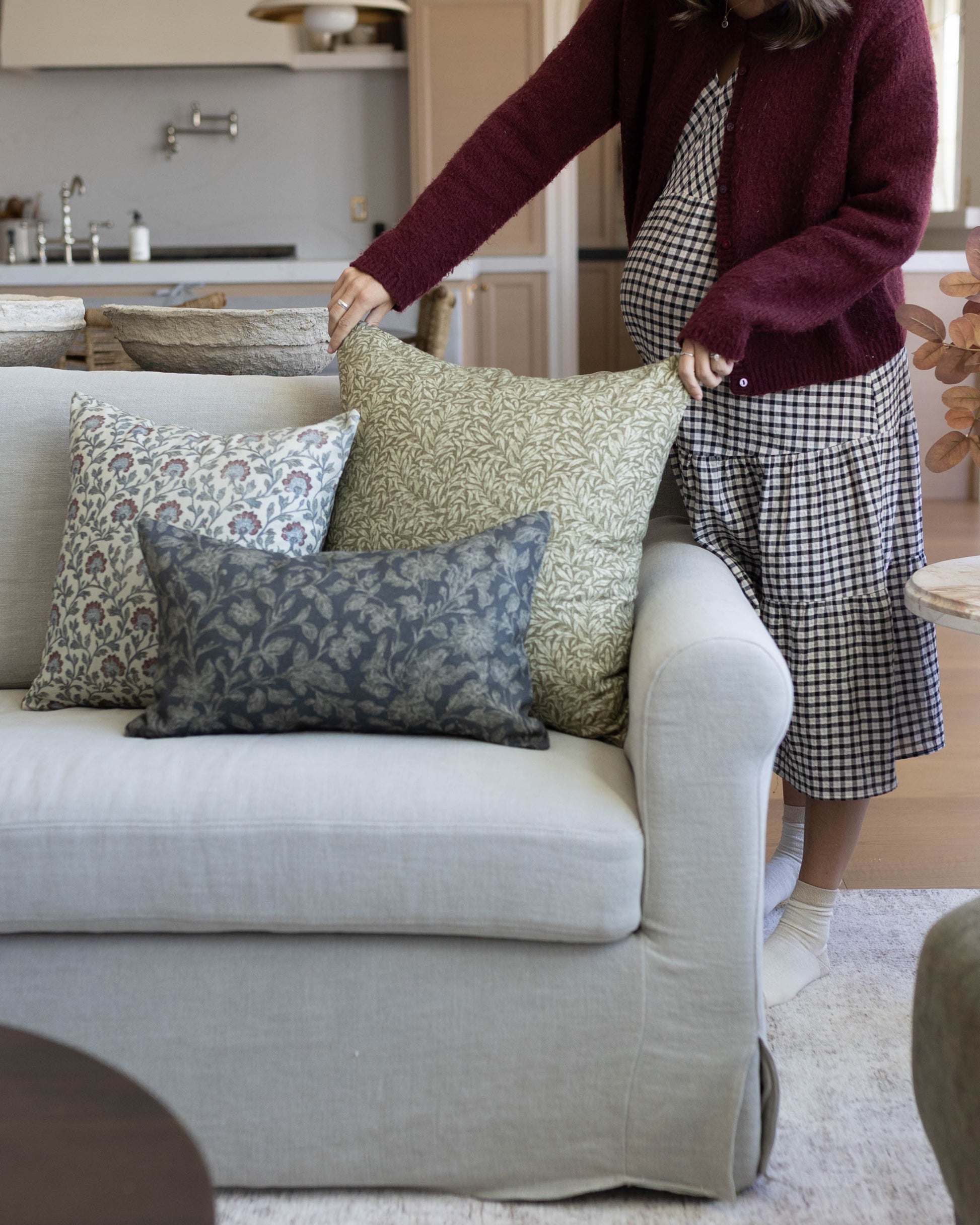 Three patterned throw pillows in green, blue, and neutral tones arranged on a cream-colored sofa.