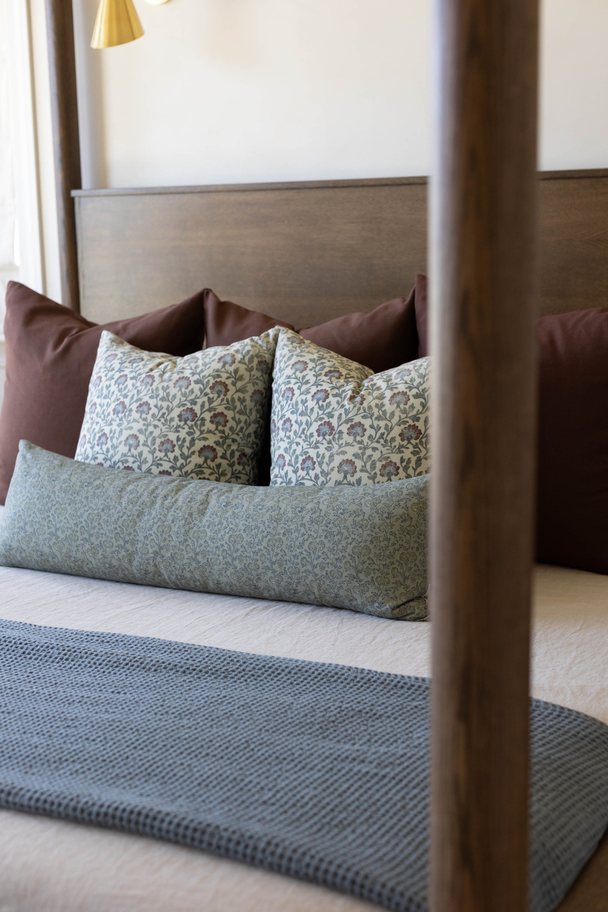 Bed with wooden frame and headboard styled with green patterned pillows, brown pillows, and gray bedding.