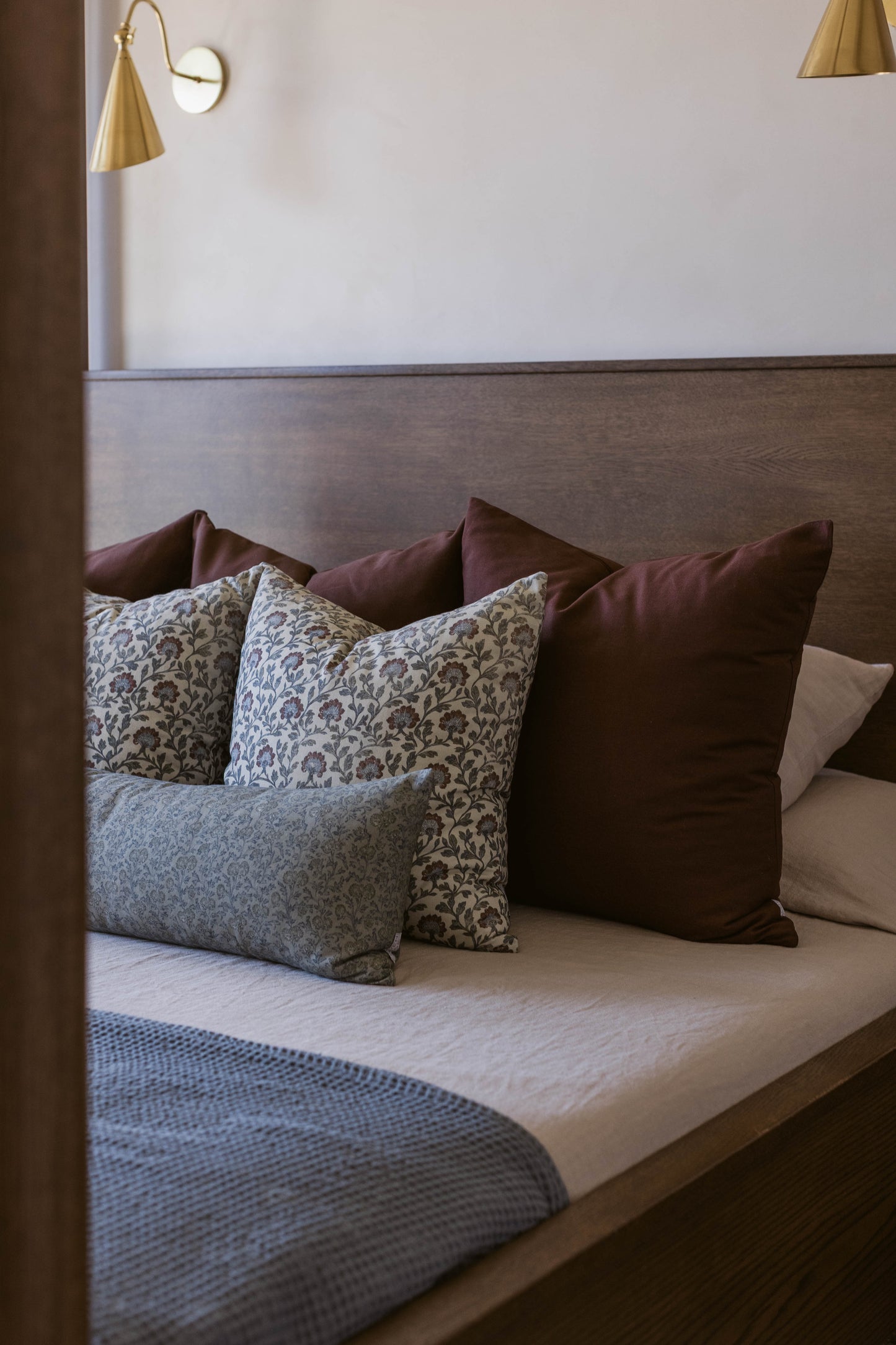Bed with upholstered headboard displaying decorative pillows in burgundy, floral, and patterned fabrics.