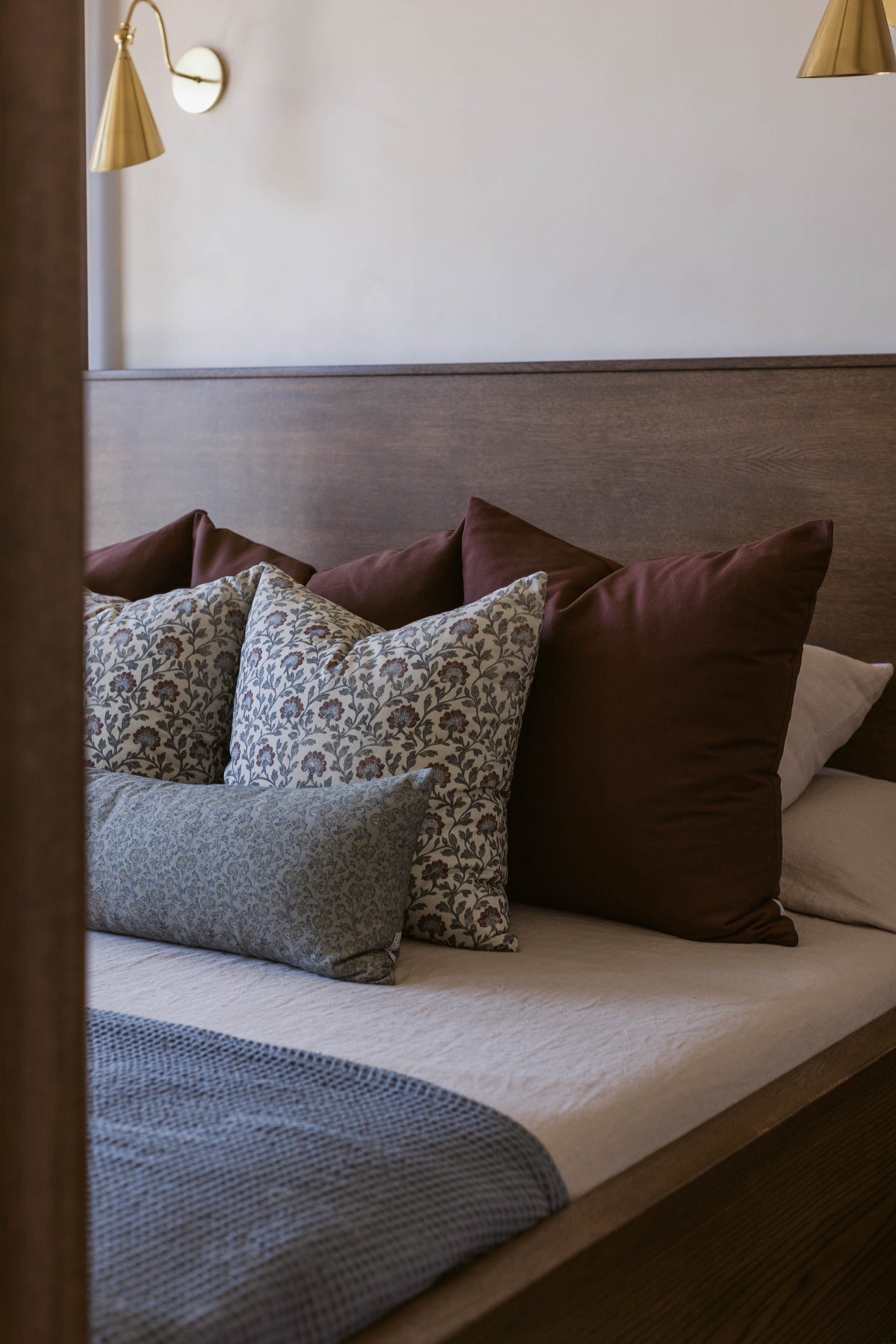 Bed with upholstered headboard displaying decorative pillows in burgundy, floral, and patterned fabrics.