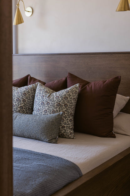 Bed with upholstered headboard displaying decorative pillows in burgundy, floral, and patterned fabrics.