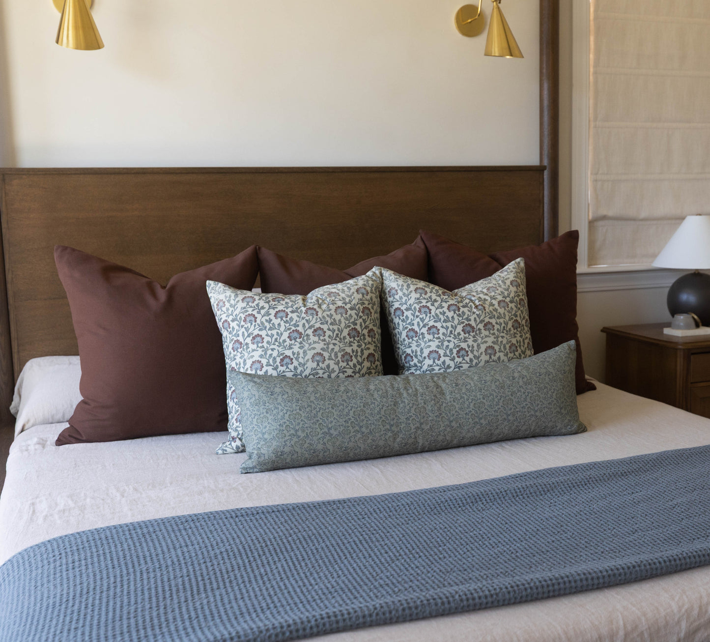 Green patterned lumbar pillow on bed with brown and patterned square pillows and gray bedding.