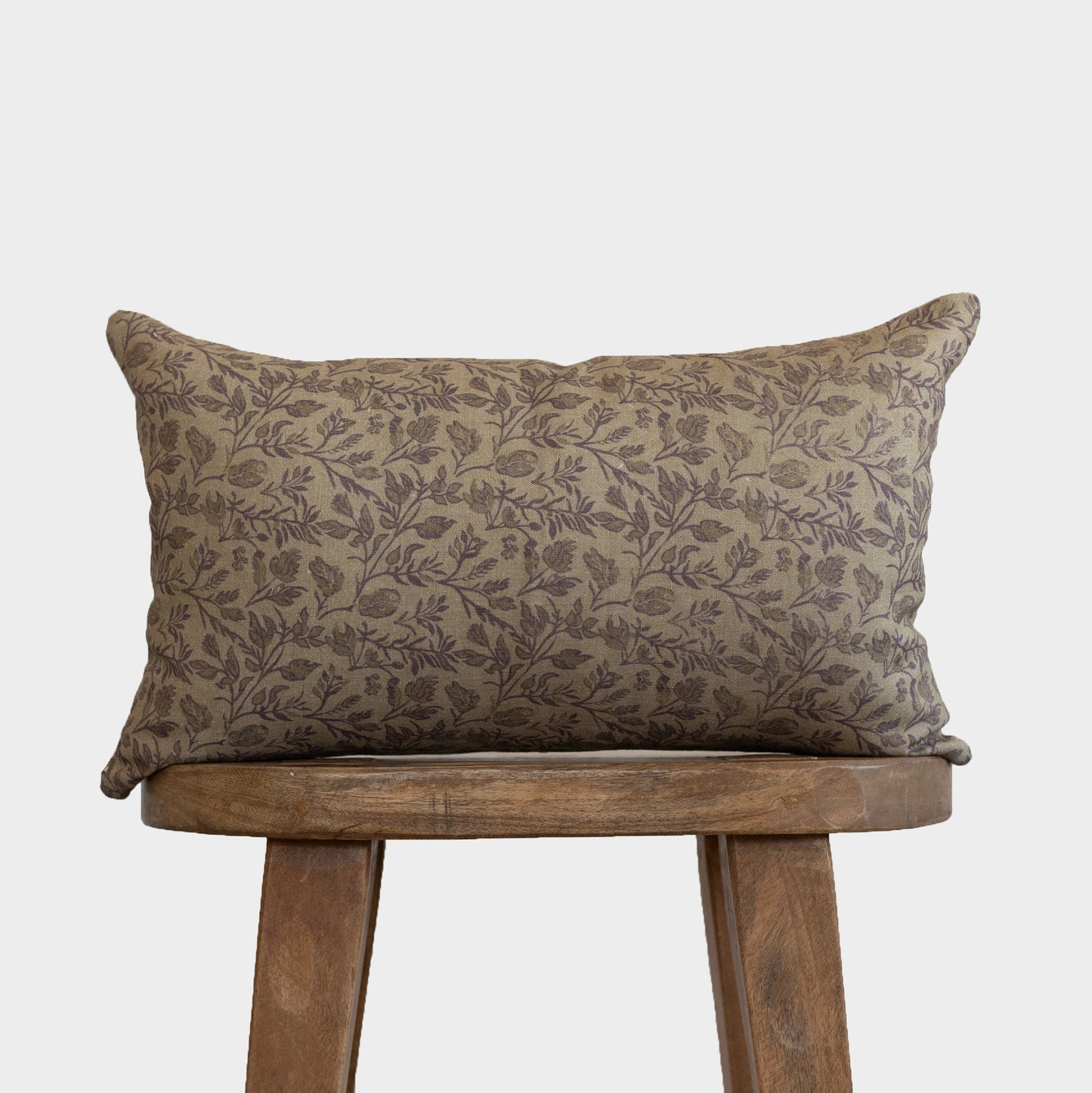 Rectangular pillow with taupe botanical print pattern on wooden stool.