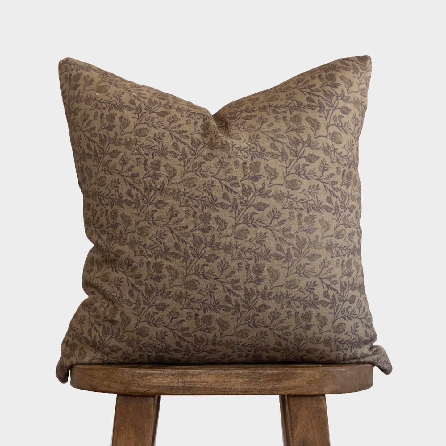 Faye pillow with tan and brown leaf pattern displayed on wooden stool.