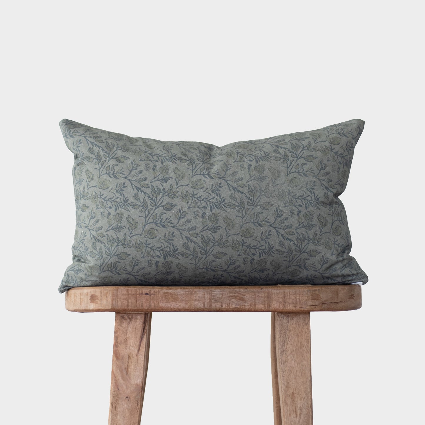 Blue floral patterned pillow with botanical print on wooden stool against white background.
