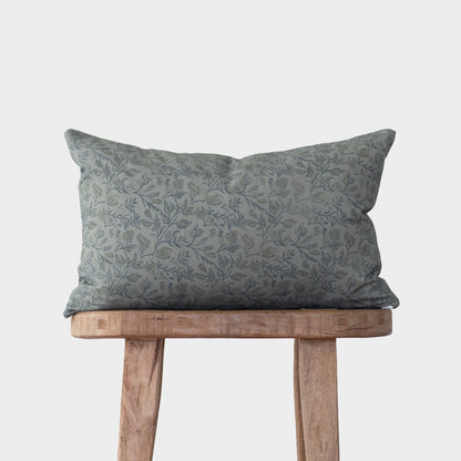 Blue floral patterned pillow with botanical print on wooden stool against white background.