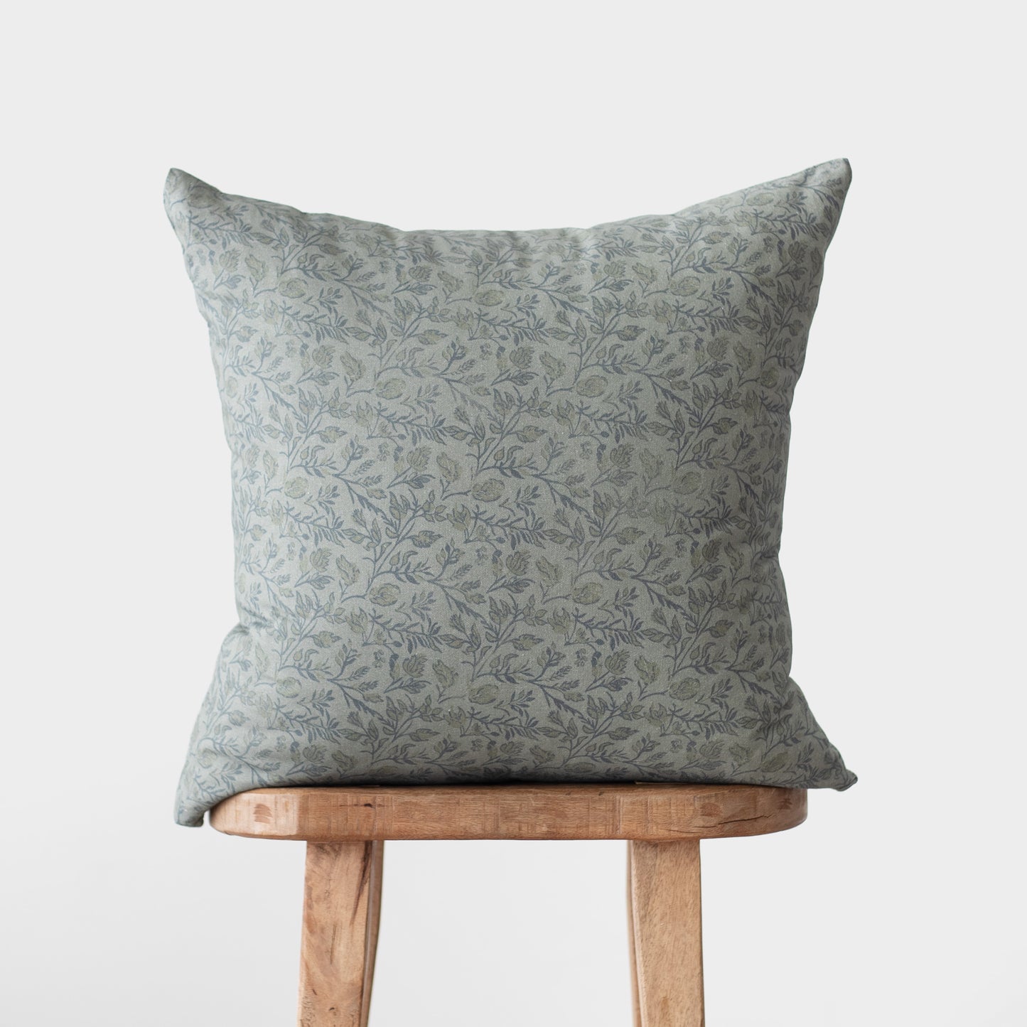 Blue-gray floral patterned throw pillow displayed on a wooden stool.