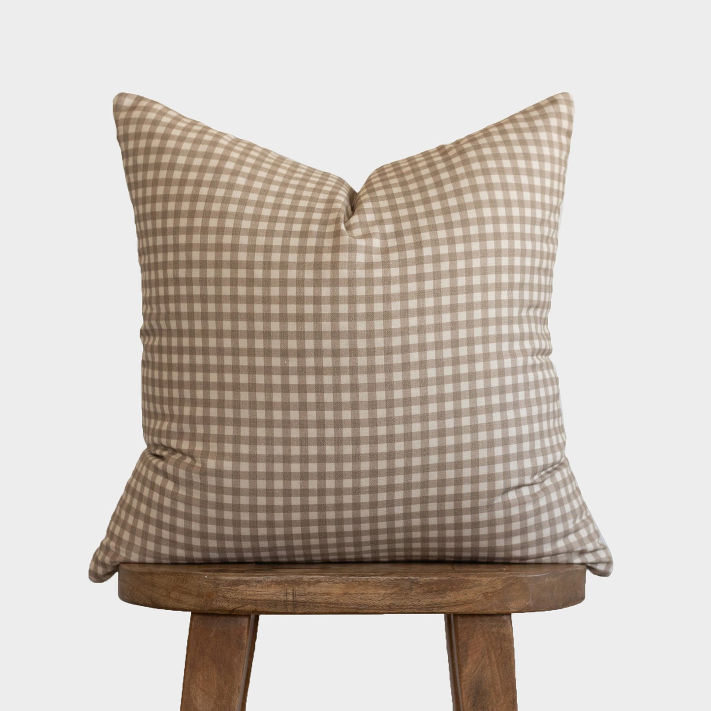 Tan and white gingham patterned pillow cover on wooden stool.