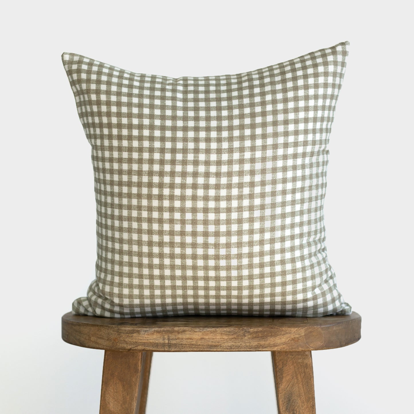 Sage green and white gingham check pillow displayed on a wooden stool.