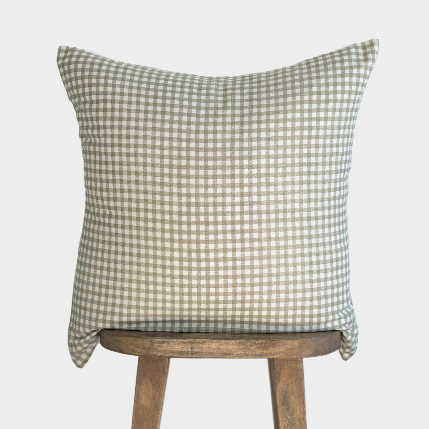 Sage and white gingham patterned pillow cover draped over wooden stool back.
