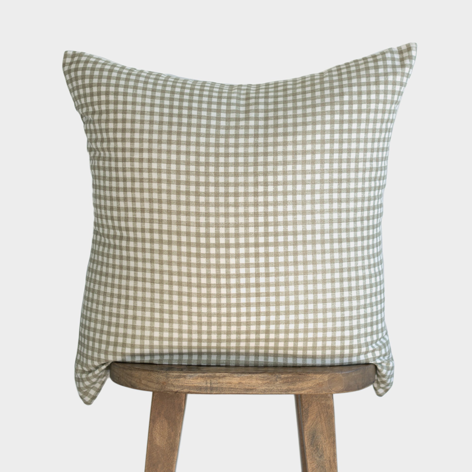Sage and white gingham patterned pillow cover draped over wooden stool back.