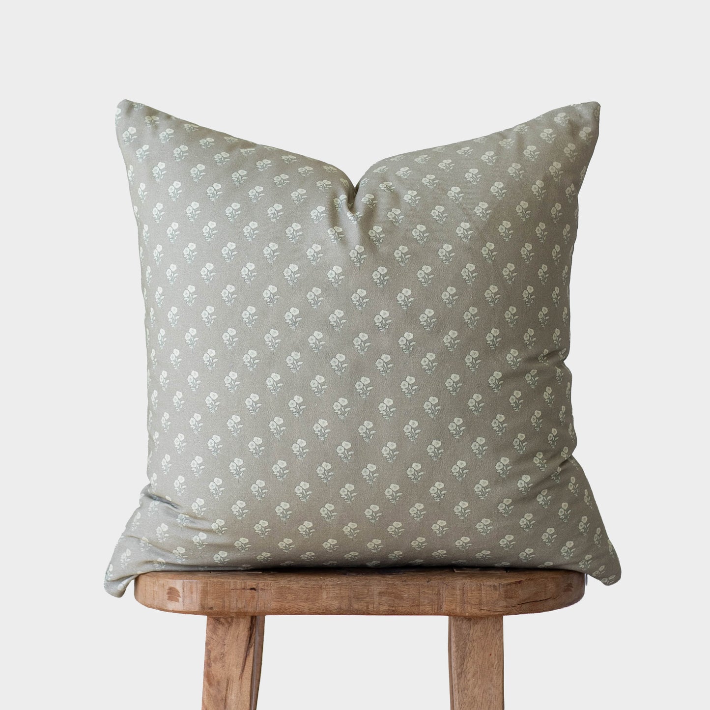 Sage green pillow with small white floral pattern, displayed on wooden stool.