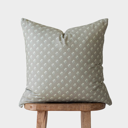 Sage green pillow with small white floral pattern, displayed on wooden stool.