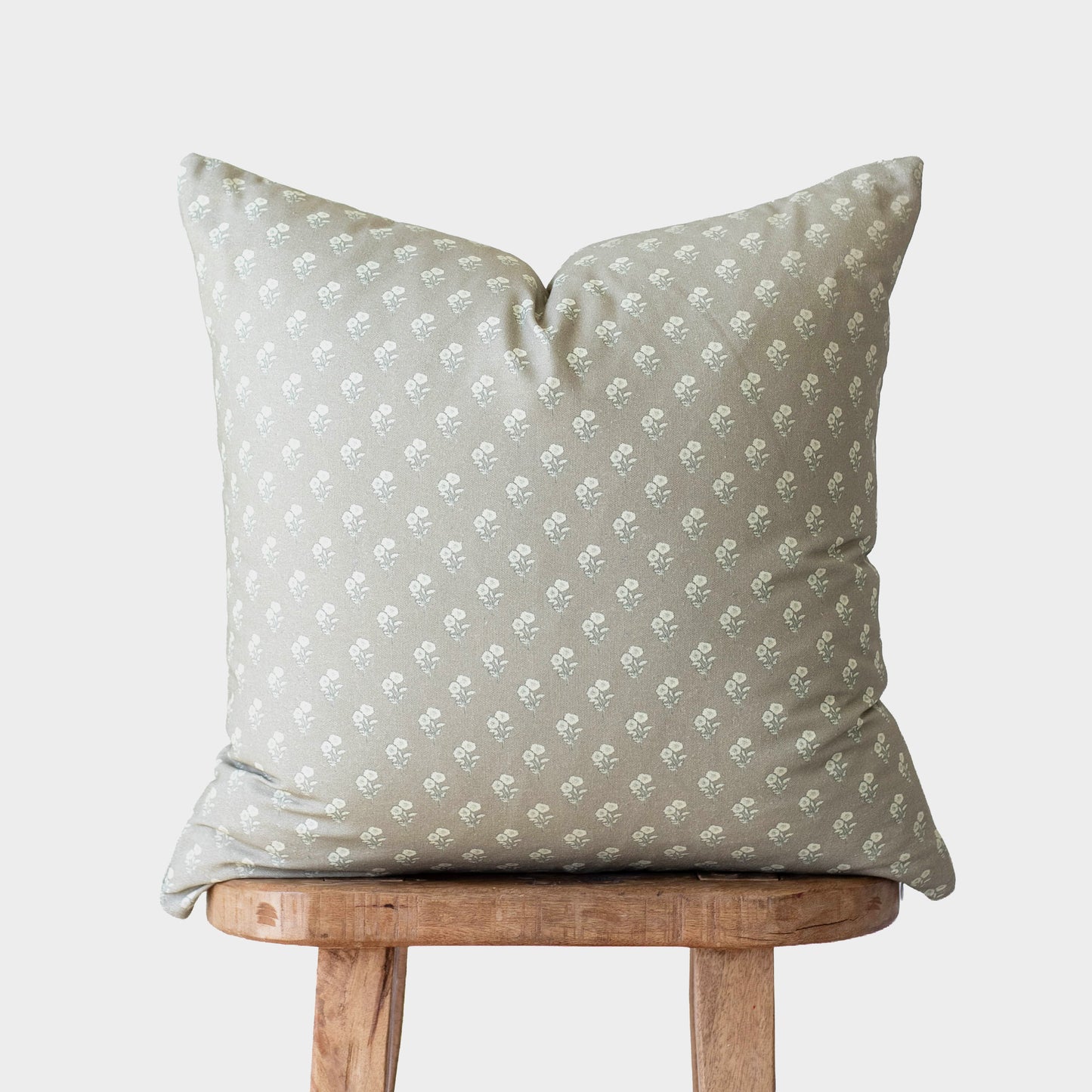 Sage green throw pillow with white floral pattern, displayed on wooden stool.