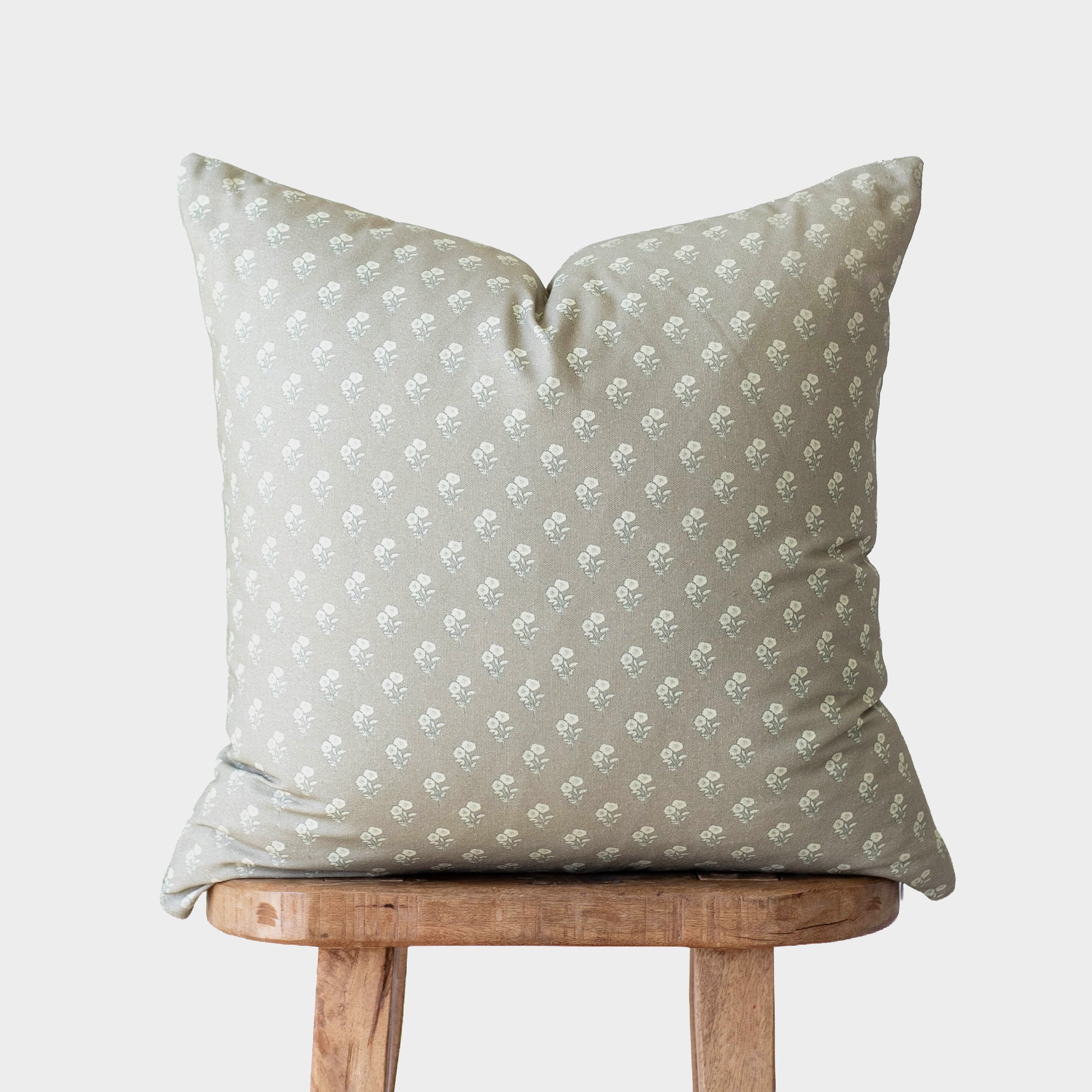 Sage green throw pillow with white floral pattern, displayed on wooden stool.