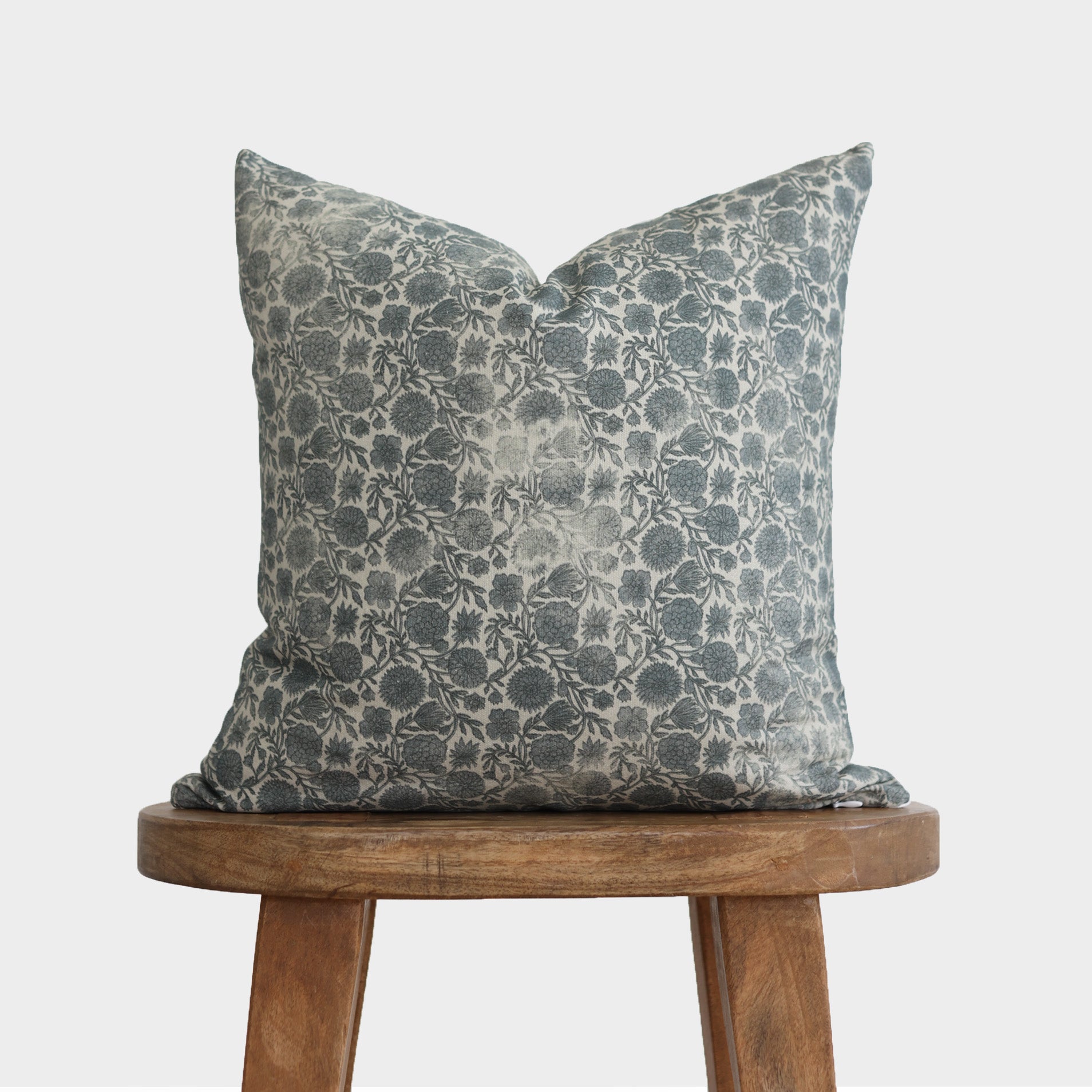 Blue-gray floral patterned throw pillow with botanical leaf design displayed on wooden stool.