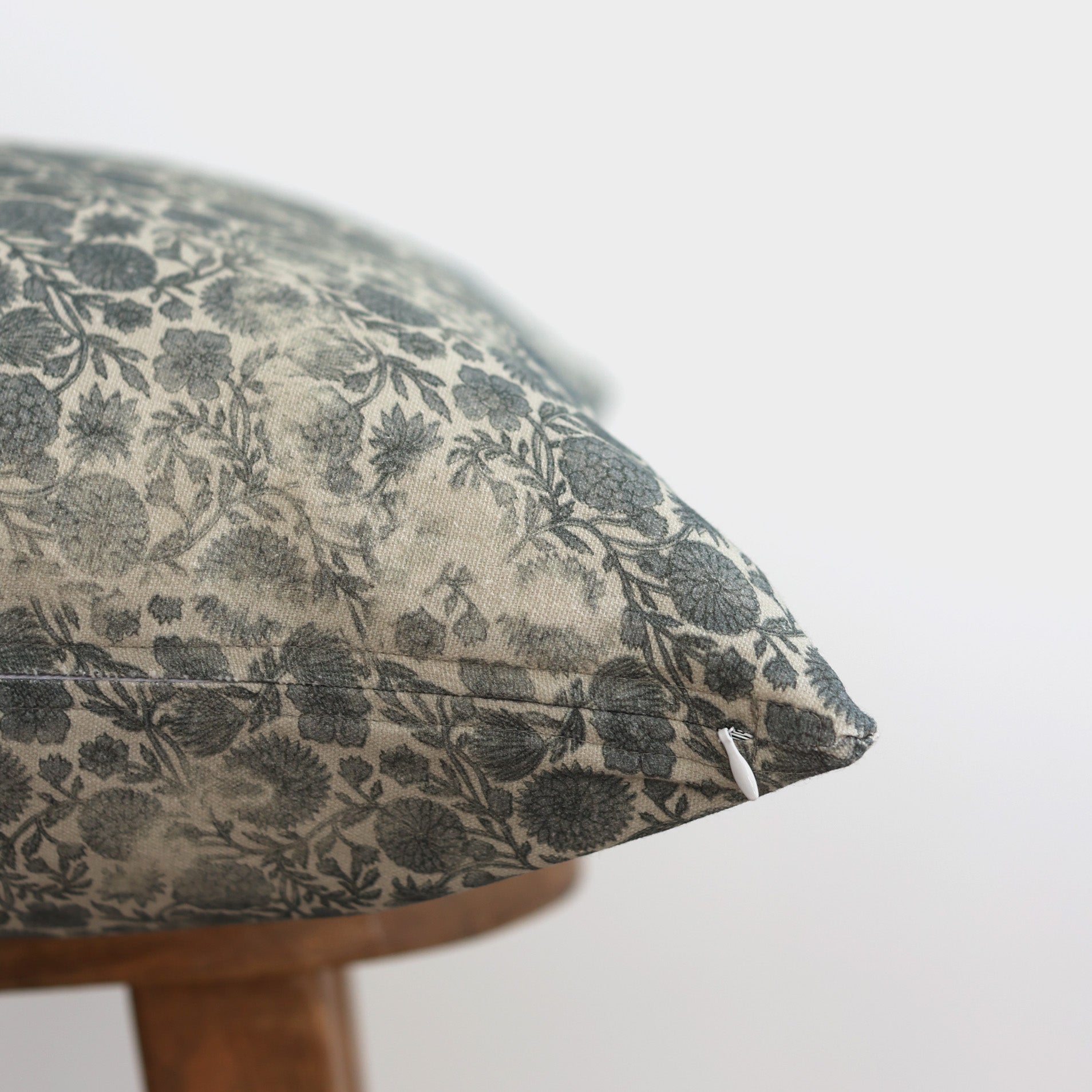 Blue floral patterned round pillow with cream background on wooden base, close-up corner view.