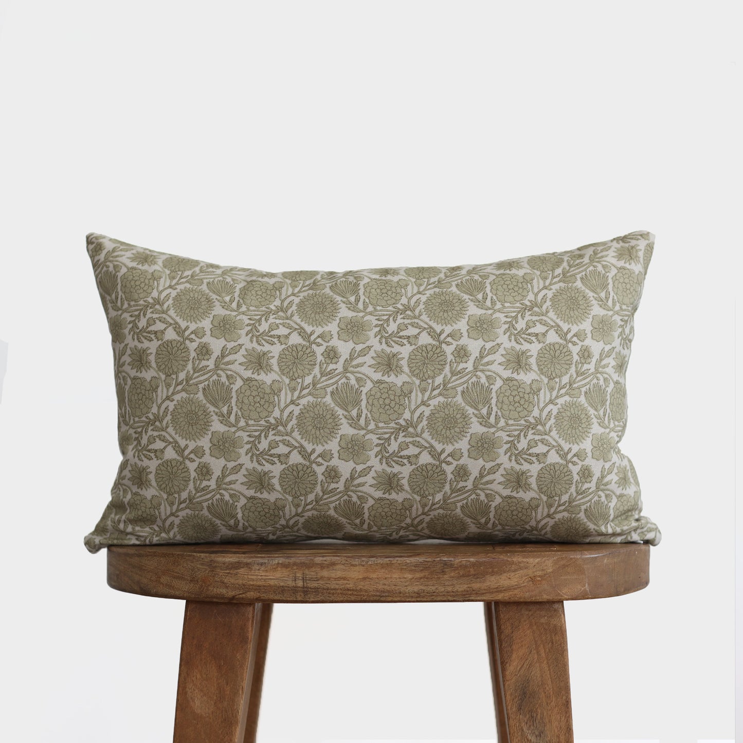 Green and cream lumbar pillow with floral botanical print, displayed on wooden stool.