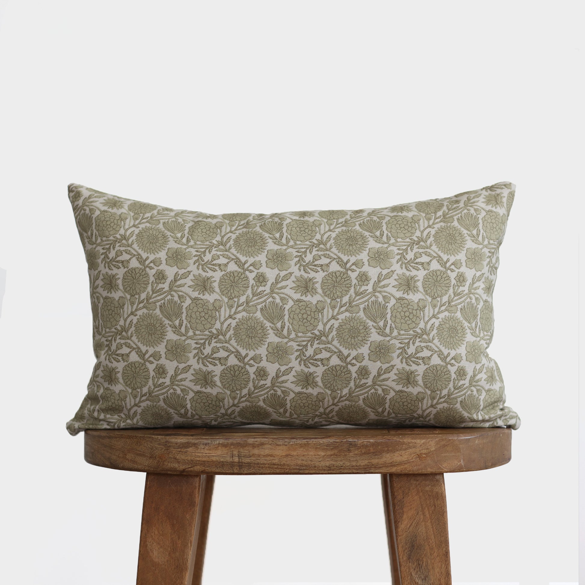 Green and cream lumbar pillow with floral botanical print, displayed on wooden stool.