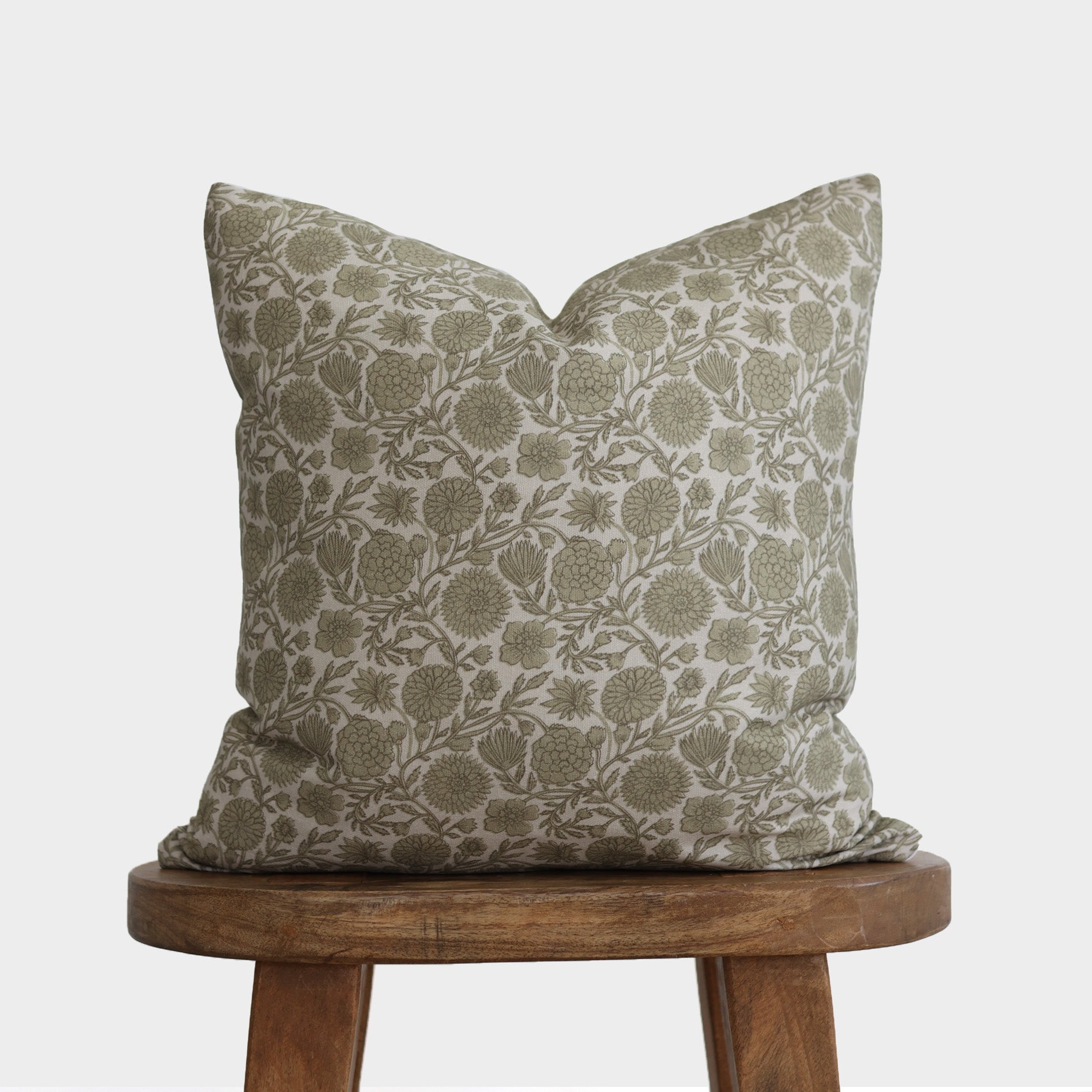 Cream and sage green floral patterned pillow with botanical print displayed on wooden stool.