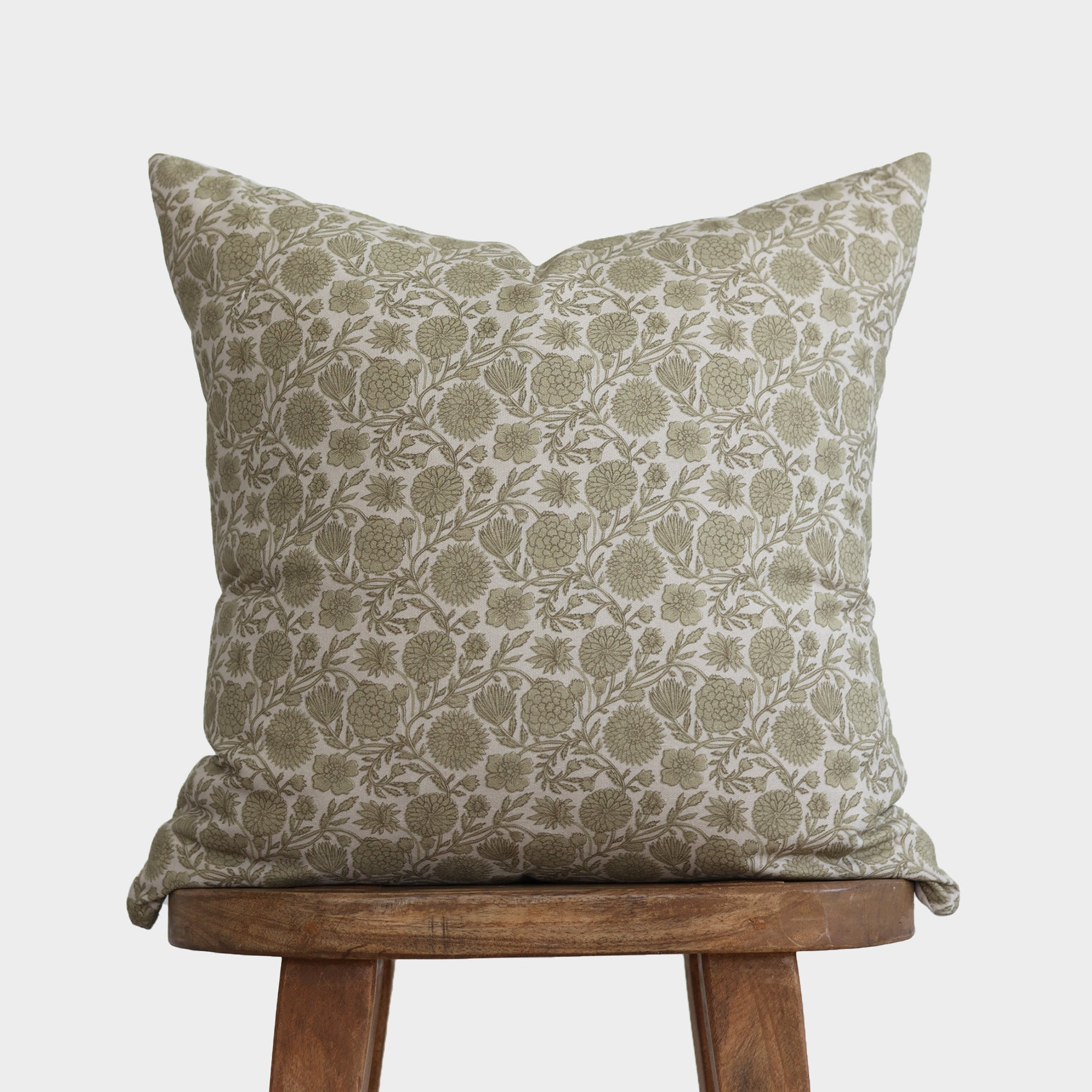 Square cushion with green and cream floral botanical print, displayed on wooden stool.