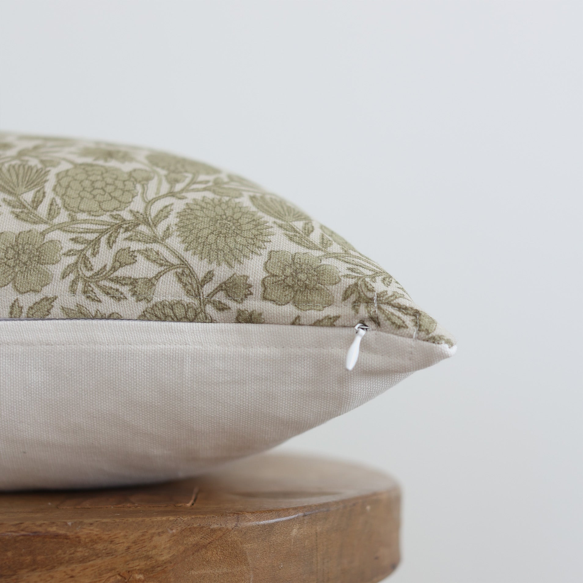 Green and cream floral patterned lumbar pillow with solid cream back and zipper closure, displayed on wooden base.