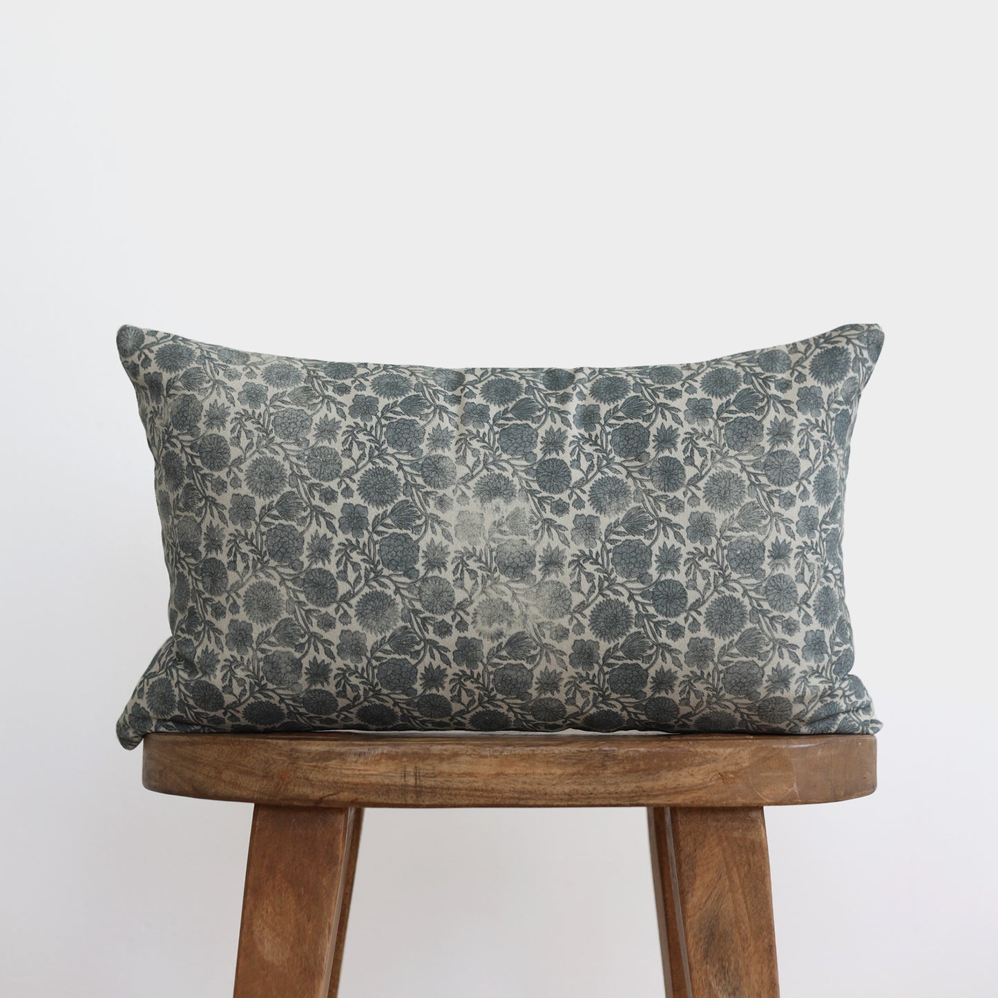 Blue and cream floral patterned lumbar pillow displayed on a wooden chair.