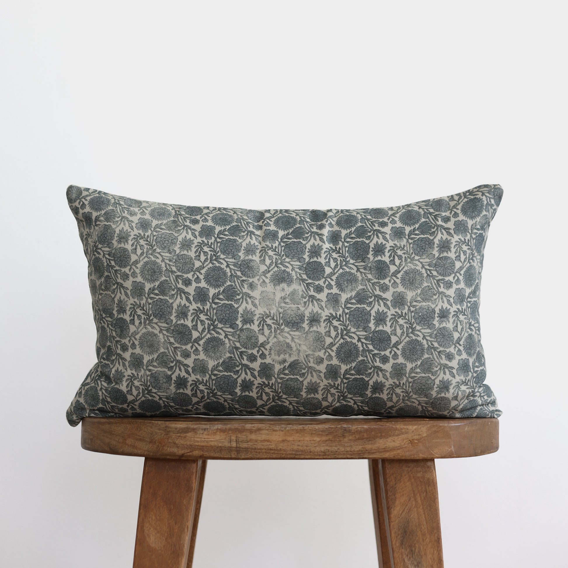 Blue and cream floral patterned lumbar pillow displayed on a wooden chair.