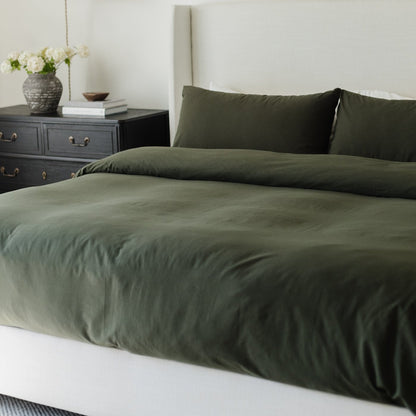 King-size olive duvet cover set on bed with matching pillows and dark nightstand with flowers.