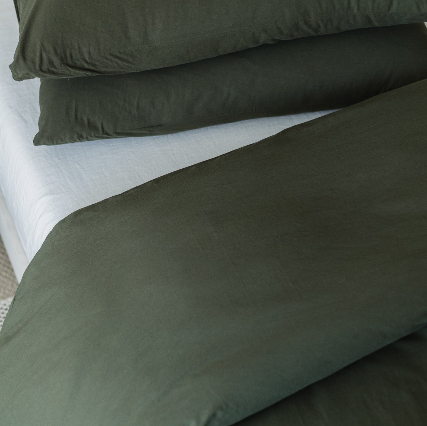 Olive green duvet cover and two matching pillowcases on a bed with white sheet.